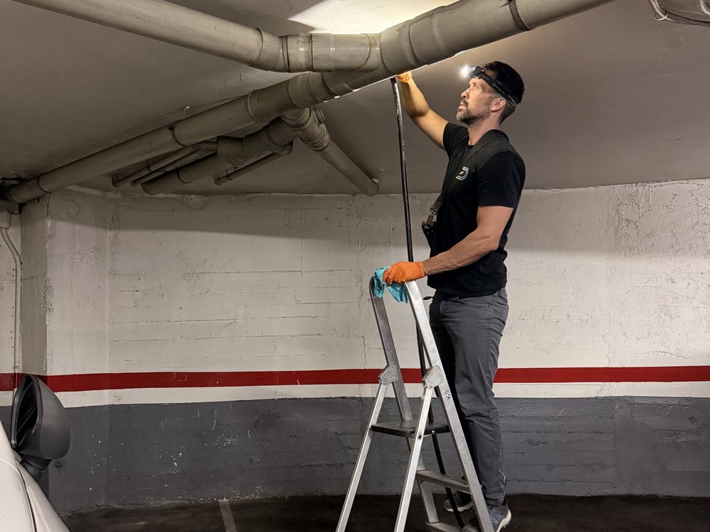 Desatasco de un tubo que cruza el techo de un parking, subido a una escalera con linterna frontal
