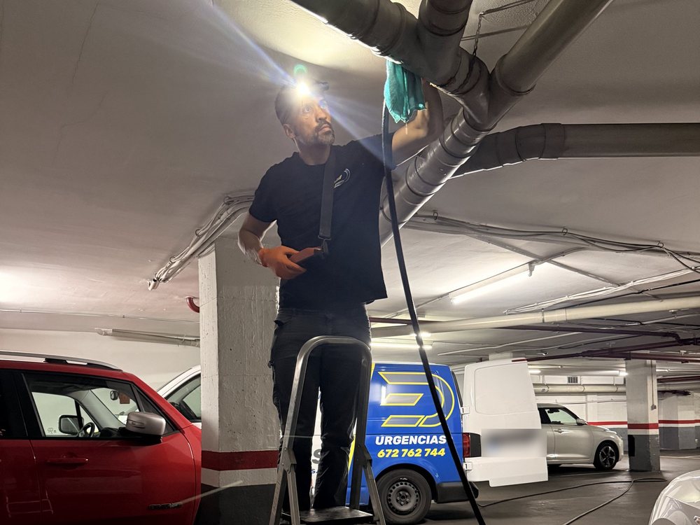 La furgoneta de Desatascos Ecoembus dentro de un parking y la manguera hasta un tubo del techo